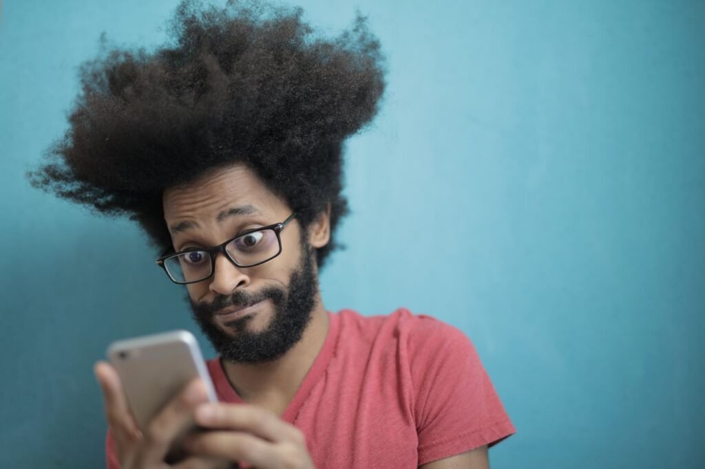 Crafting Captivating Headlines: Your awesome post title goes here A surprised man with afro hair and glasses looks at his smartphone against a blue background.